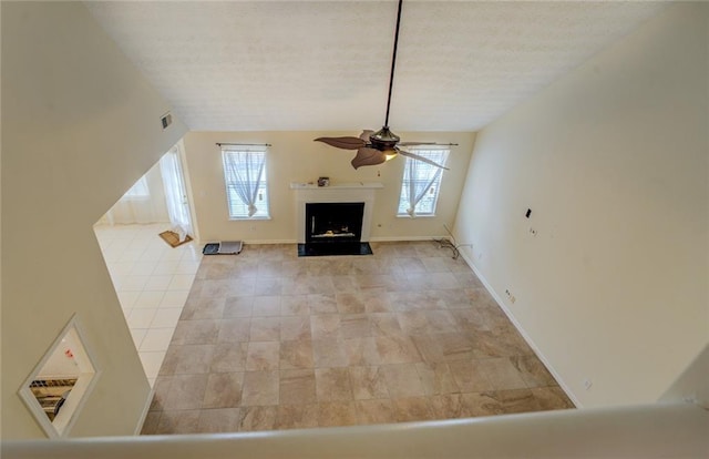 unfurnished living room featuring ceiling fan, a fireplace, baseboards, and vaulted ceiling