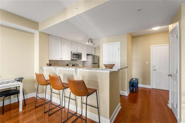 kitchen featuring backsplash, kitchen peninsula, a kitchen bar, white cabinetry, and stainless steel appliances