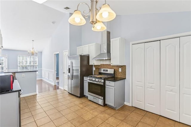 kitchen featuring light tile patterned floors, dark countertops, wall chimney exhaust hood, stainless steel appliances, and a chandelier