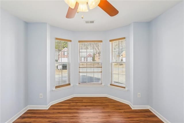empty room featuring wood finished floors, visible vents, baseboards, and ceiling fan