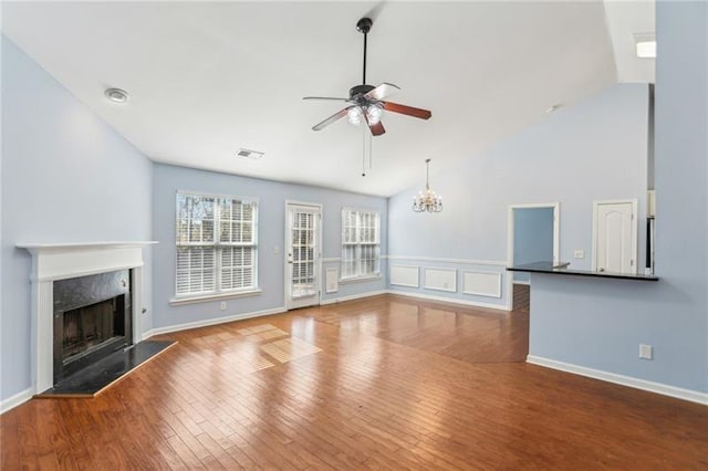 unfurnished living room featuring wood finished floors, ceiling fan with notable chandelier, a wainscoted wall, visible vents, and a high end fireplace