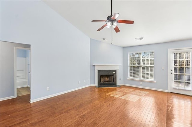 unfurnished living room with a healthy amount of sunlight, ceiling fan, visible vents, a fireplace with flush hearth, and wood finished floors