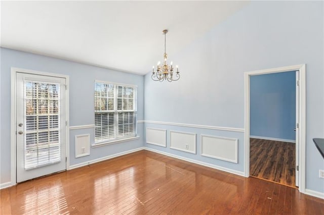 unfurnished dining area featuring baseboards, vaulted ceiling, a notable chandelier, and wood finished floors