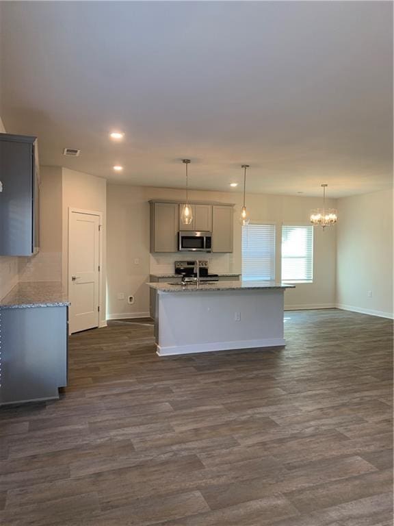 kitchen with dark wood-type flooring, decorative light fixtures, appliances with stainless steel finishes, gray cabinets, and light stone countertops