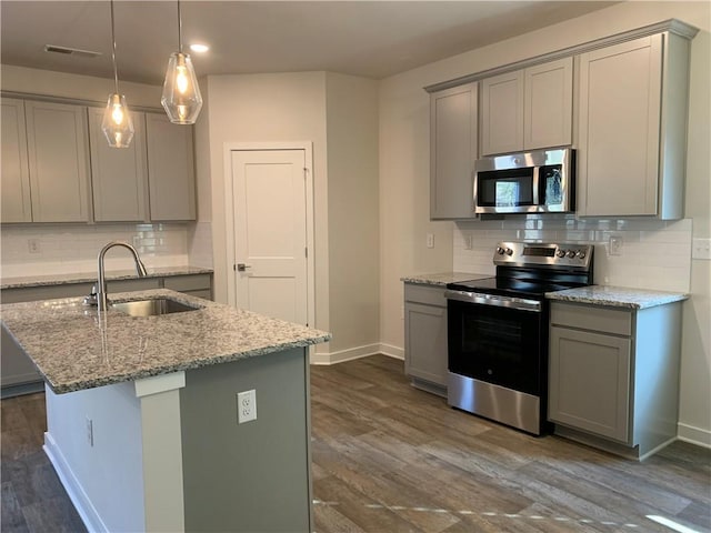 kitchen with light stone counters, stainless steel appliances, an island with sink, and gray cabinetry