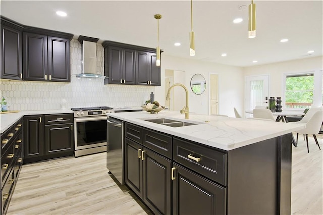 kitchen featuring hanging light fixtures, sink, wall chimney exhaust hood, an island with sink, and appliances with stainless steel finishes