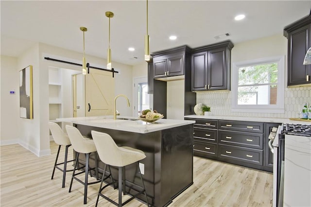 kitchen with pendant lighting, a kitchen island with sink, gas range, a barn door, and light hardwood / wood-style floors