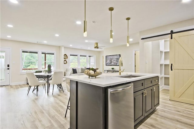 kitchen featuring stainless steel dishwasher, sink, a barn door, a center island with sink, and hanging light fixtures