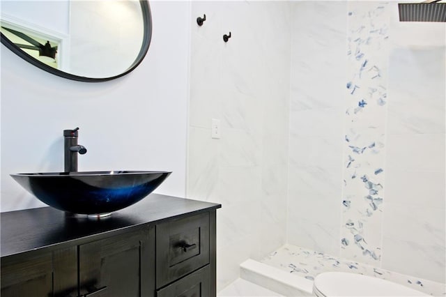 bathroom with a tile shower, vanity, and toilet