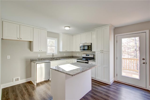 kitchen with light stone countertops, stainless steel appliances, sink, white cabinets, and a center island