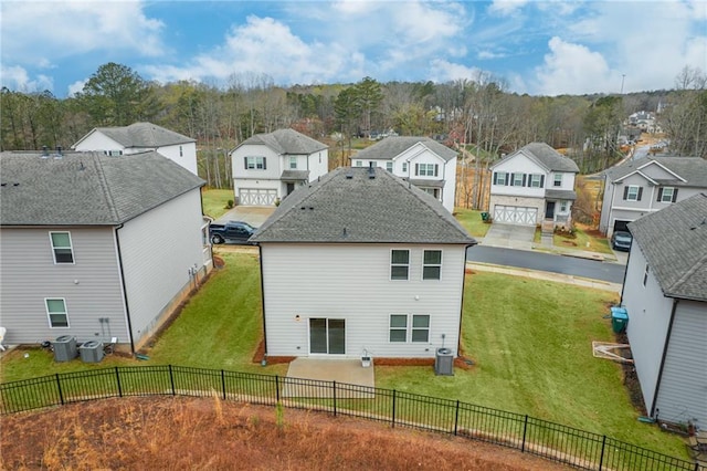 back of property with a fenced backyard, a residential view, central AC unit, and a lawn
