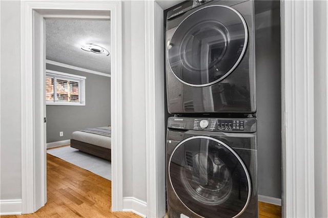 clothes washing area featuring hardwood / wood-style flooring, ornamental molding, a textured ceiling, and stacked washer and clothes dryer