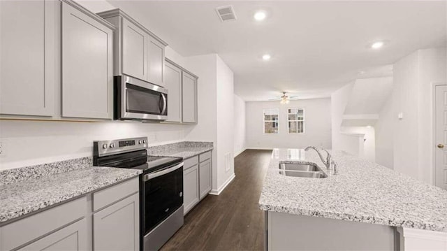 kitchen with stainless steel appliances, dark hardwood / wood-style flooring, sink, ceiling fan, and a center island with sink