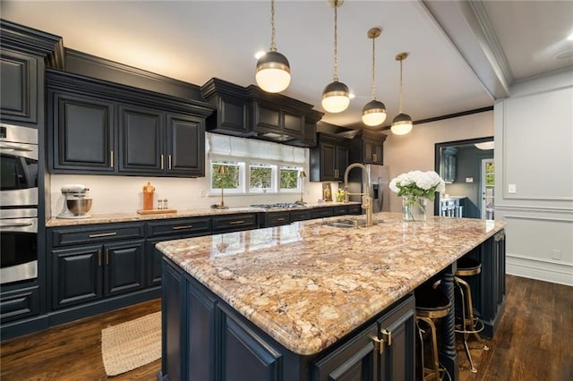 kitchen featuring an island with sink, a kitchen breakfast bar, crown molding, double oven, and a sink