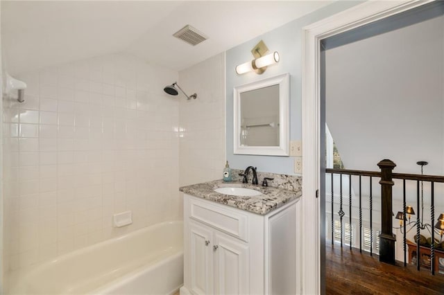 bathroom with visible vents, wood finished floors, vaulted ceiling, vanity, and shower / bathing tub combination