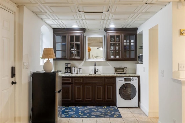 kitchen featuring freestanding refrigerator, washer / clothes dryer, a sink, and dark brown cabinetry