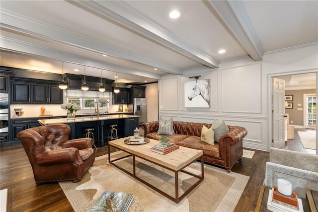 living area with beam ceiling, crown molding, recessed lighting, a decorative wall, and wood finished floors