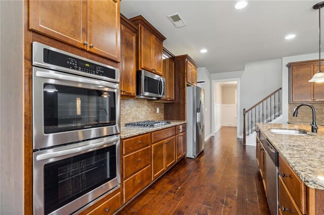 kitchen featuring light stone counters, stainless steel appliances, pendant lighting, sink, and dark wood-type flooring