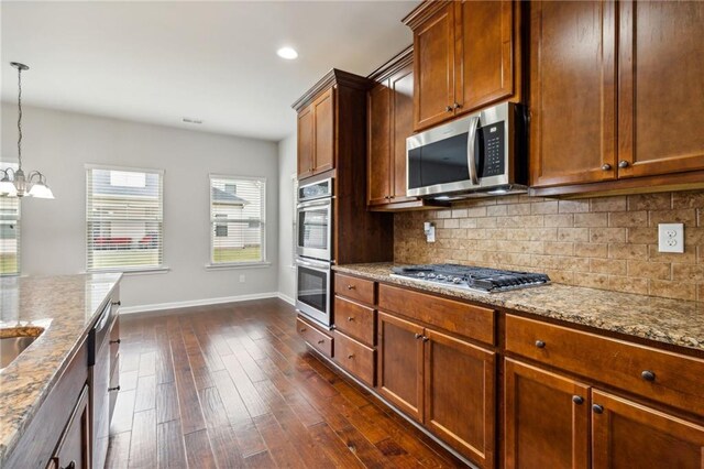 kitchen featuring light stone counters, stainless steel appliances, dark hardwood / wood-style flooring, pendant lighting, and a chandelier