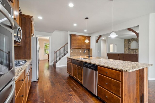 kitchen featuring sink, appliances with stainless steel finishes, light stone countertops, hanging light fixtures, and dark hardwood / wood-style flooring