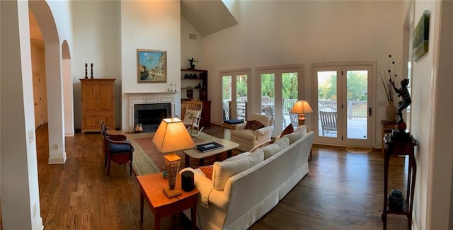 living room featuring dark wood finished floors, a tiled fireplace, arched walkways, and a towering ceiling
