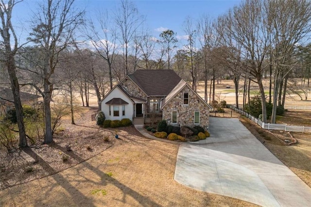 view of front of home featuring stone siding, fence, and concrete driveway