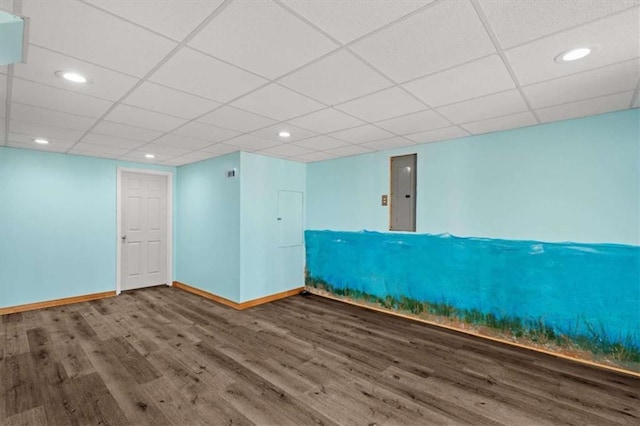 basement featuring electric panel, a drop ceiling, baseboards, and wood finished floors