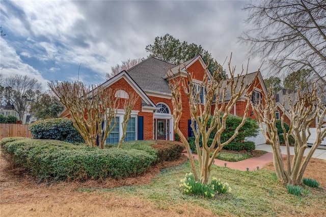 traditional-style home with driveway, a garage, a shingled roof, fence, and brick siding