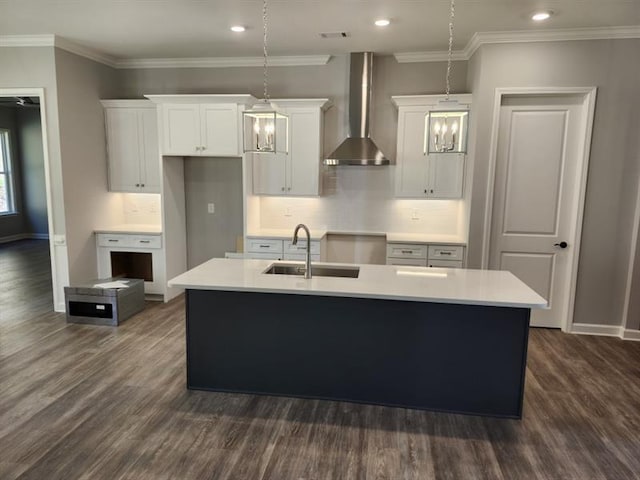 kitchen featuring light countertops, wall chimney range hood, a sink, and a kitchen island with sink