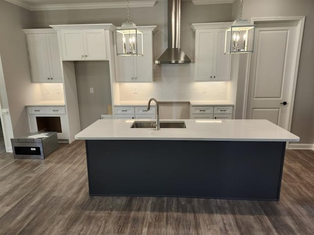 kitchen featuring an island with sink, wall chimney exhaust hood, light countertops, and a sink