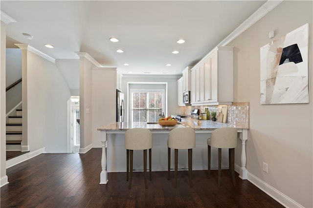 kitchen with dark wood-type flooring, kitchen peninsula, appliances with stainless steel finishes, a kitchen bar, and white cabinetry