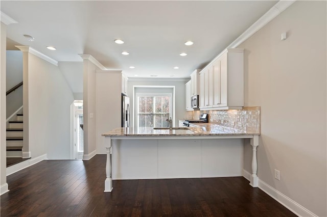 kitchen with kitchen peninsula, appliances with stainless steel finishes, dark hardwood / wood-style flooring, decorative backsplash, and white cabinetry