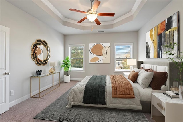 carpeted bedroom with ceiling fan, crown molding, a tray ceiling, and multiple windows