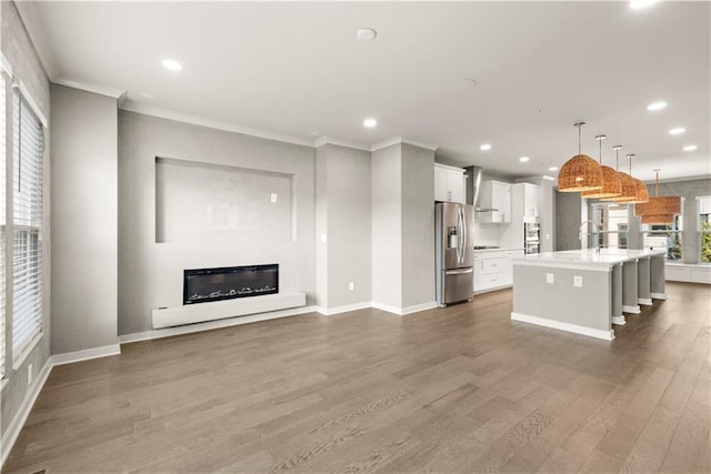 kitchen featuring stainless steel appliances, wood-type flooring, decorative light fixtures, a center island with sink, and white cabinetry