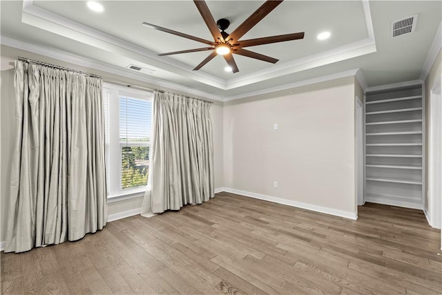 spare room with a raised ceiling, ornamental molding, and light hardwood / wood-style flooring