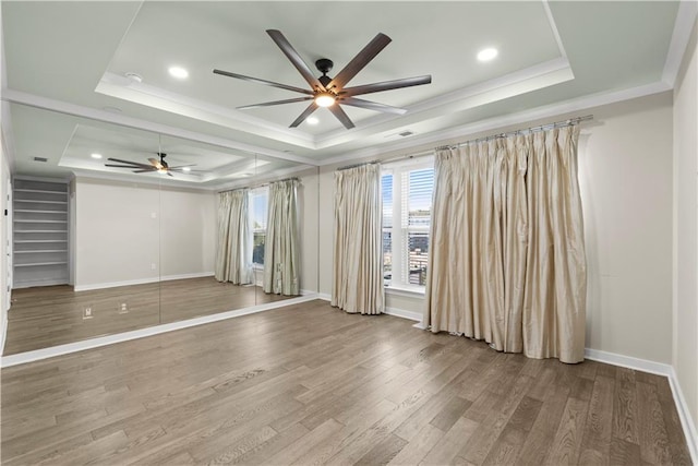 empty room with a raised ceiling, ceiling fan, ornamental molding, and hardwood / wood-style flooring