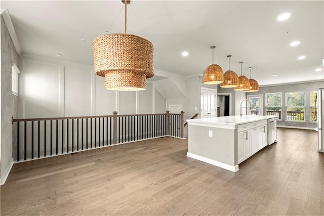 kitchen featuring pendant lighting, wood-type flooring, a center island with sink, white cabinets, and appliances with stainless steel finishes