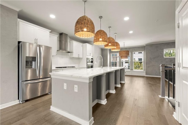 kitchen with white cabinetry, an island with sink, stainless steel appliances, and wall chimney range hood