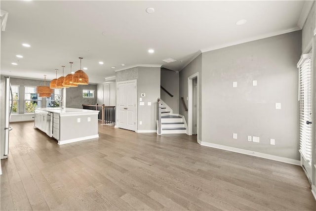 kitchen with hanging light fixtures, crown molding, hardwood / wood-style floors, a center island with sink, and white cabinets