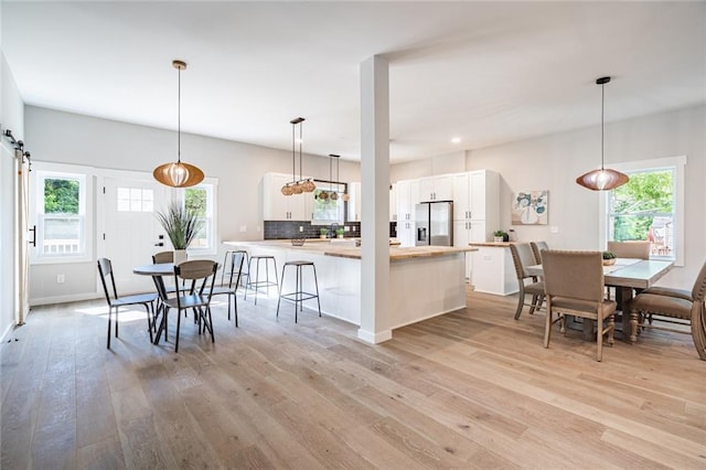 kitchen featuring decorative light fixtures, white cabinetry, backsplash, stainless steel fridge, and kitchen peninsula