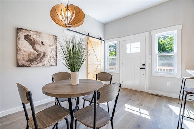 dining space with light wood-type flooring, a barn door, and a healthy amount of sunlight