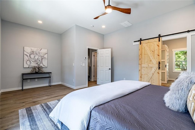 bedroom featuring dark wood-type flooring, connected bathroom, ceiling fan, and a barn door