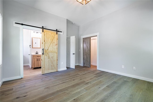 unfurnished bedroom with wood-type flooring, ensuite bath, and a barn door