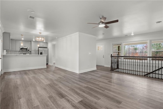 unfurnished living room featuring crown molding, ceiling fan with notable chandelier, and hardwood / wood-style floors