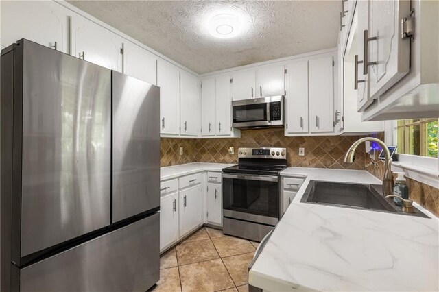 kitchen with decorative backsplash, a textured ceiling, white cabinetry, a sink, and stainless steel appliances