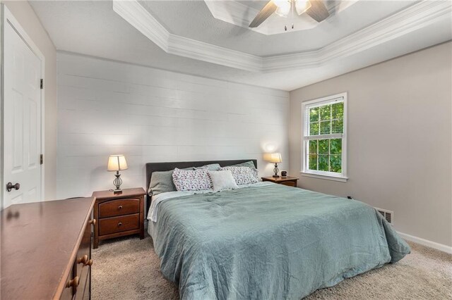 carpeted bedroom featuring ceiling fan, a raised ceiling, baseboards, visible vents, and ornamental molding