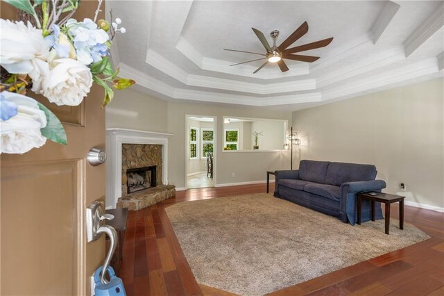 living room featuring crown molding, a raised ceiling, ceiling fan, and dark wood finished floors