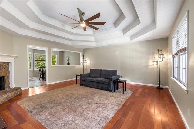 living room featuring ornamental molding, a fireplace, a tray ceiling, hardwood / wood-style flooring, and a ceiling fan