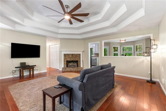 living area featuring ceiling fan, crown molding, a fireplace, a raised ceiling, and wood-type flooring