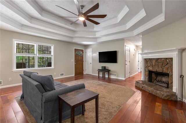 living room with ceiling fan, a raised ceiling, a fireplace, ornamental molding, and hardwood / wood-style flooring